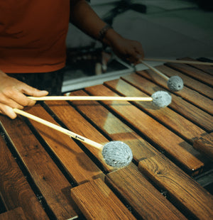 Person playing a marimba with mallets on a wooden surface